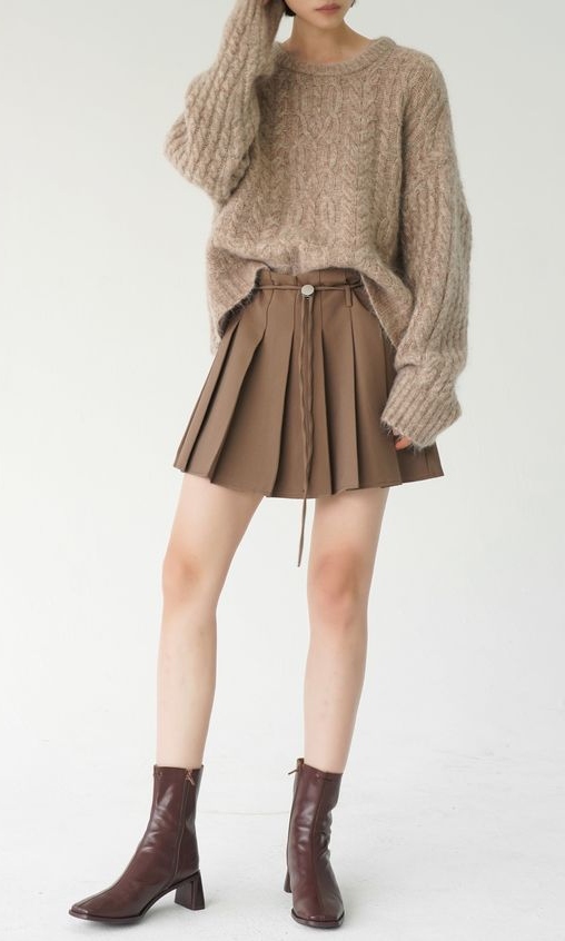 A girl wearing chunky sweater and mini skirt in a white room