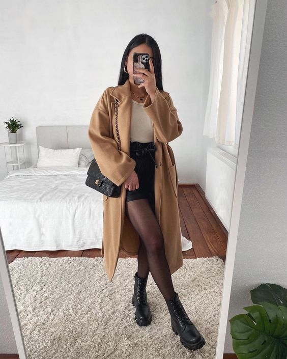 A women taking mirror selfie, showing her long coat, mini skirt, tights and ankle boots.
