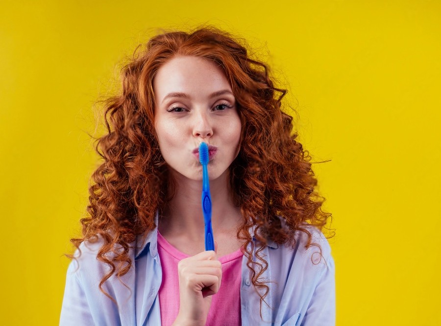 woman redhaired ginger with eco toothbrush and toothpaste on yellow studio background