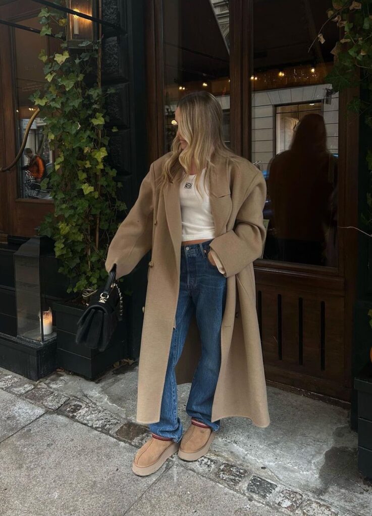 Fashion model wearing a khaki long coat with pads while holding on to black purse Infront of a coffee shop