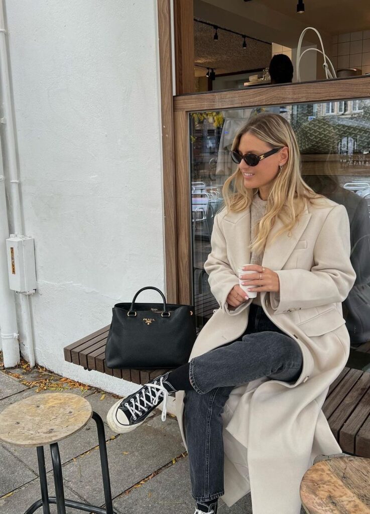 A women sitting on a bench wearing a classical everyday long coat while enjoying the coffee