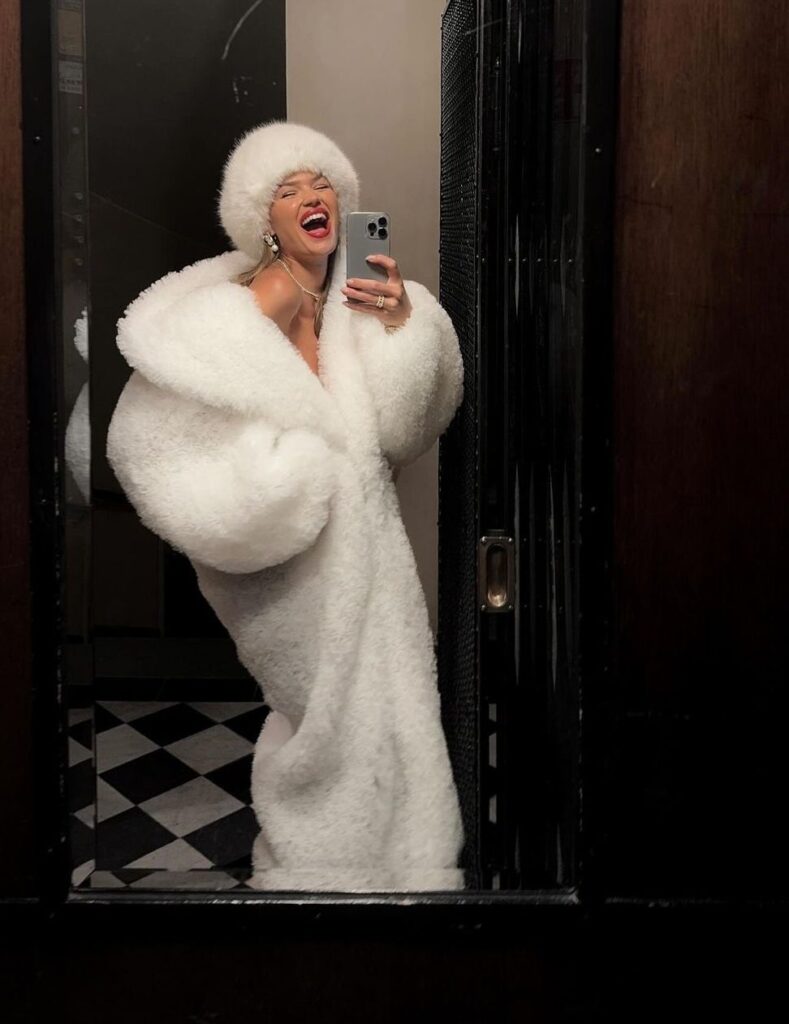Beautiful girl wearing a white fur long coat, hat Infront of a mirror